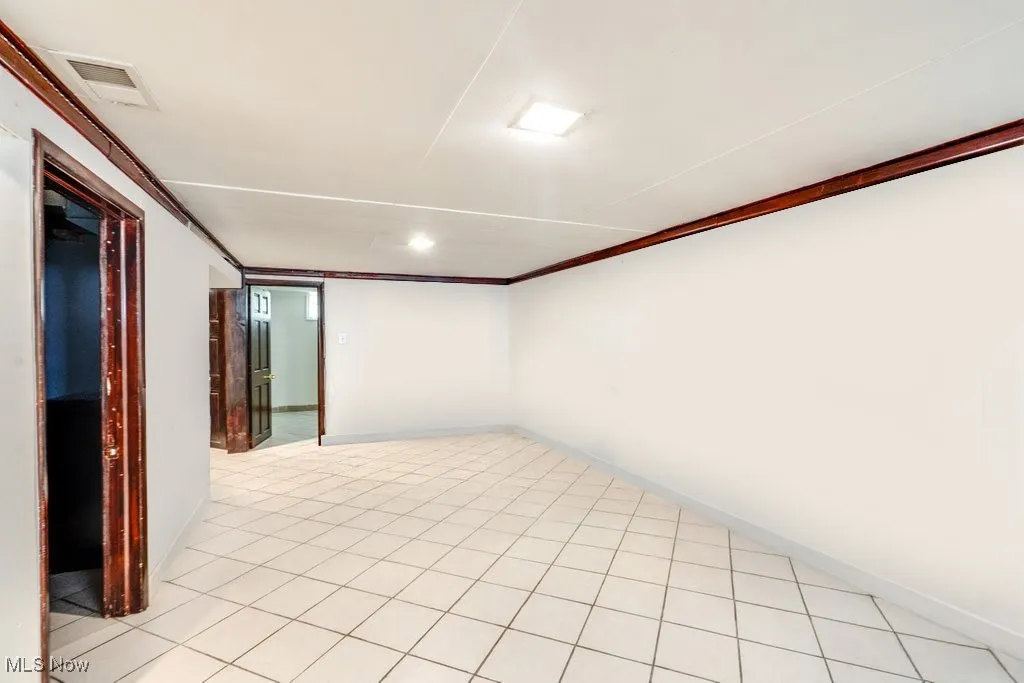 Empty room featuring light tile patterned flooring and crown molding