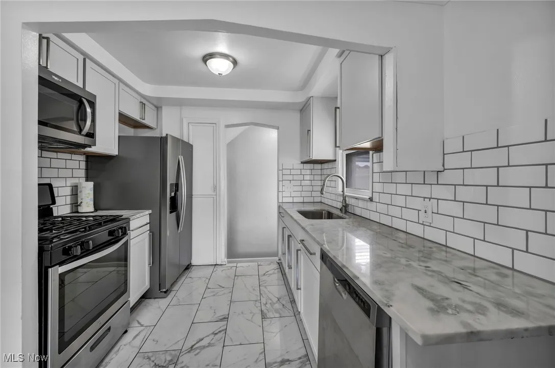 Kitchen with appliances with stainless steel finishes, light marble finish flooring, tasteful backsplash, light stone countertops, and white cabinets