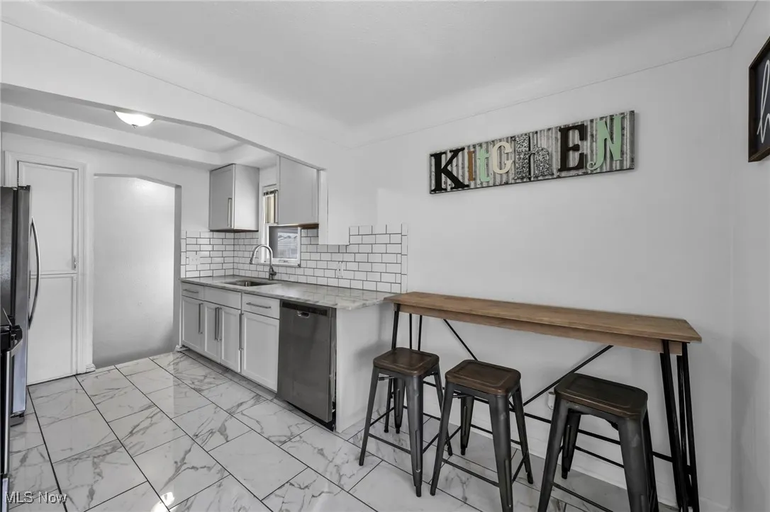 Kitchen with backsplash, light marble finish floors, appliances with stainless steel finishes, a breakfast bar, and light stone counters