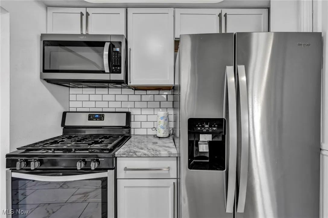 Kitchen with stainless steel appliances, backsplash, white cabinets, and light stone counters