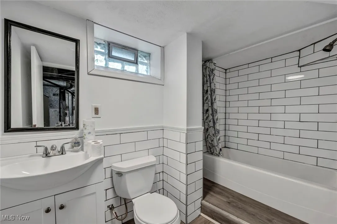 Full bath with vanity, shower / tub combo with curtain, wood finished floors, tile walls, and a wainscoted wall