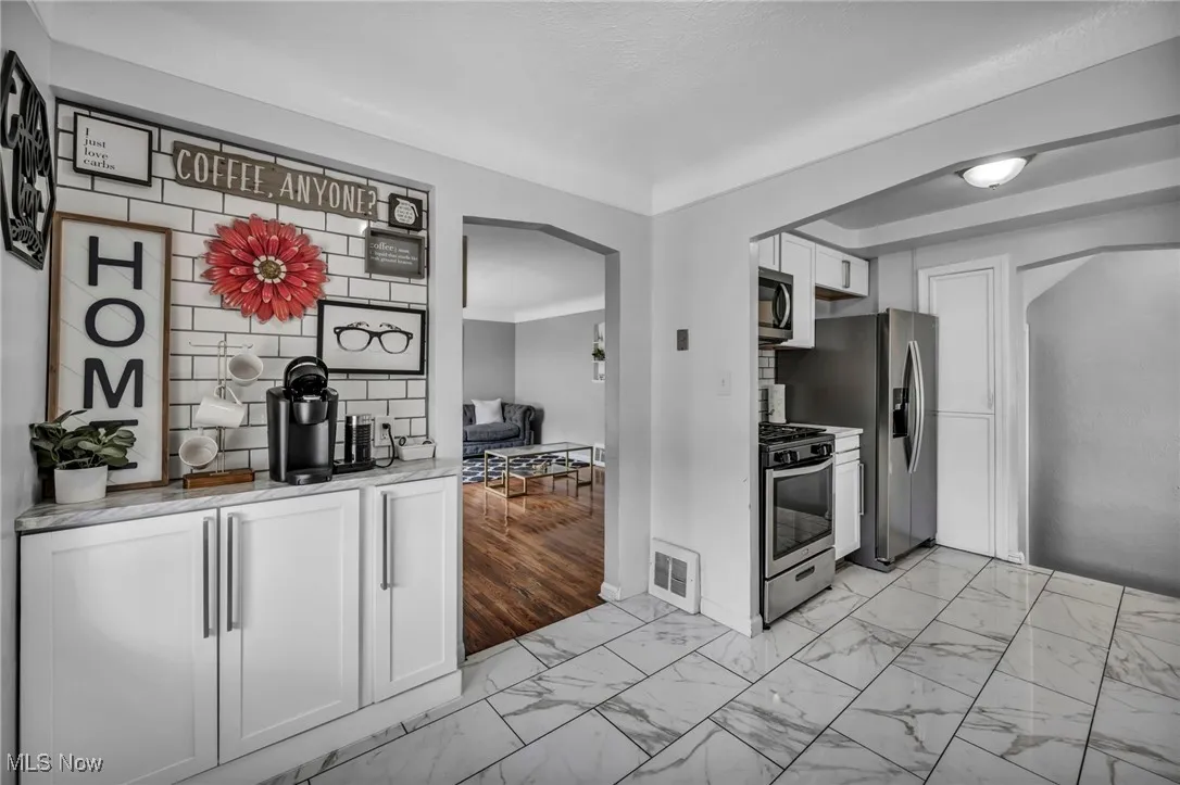 Kitchen with light marble finish flooring, arched walkways, appliances with stainless steel finishes, and white cabinetry