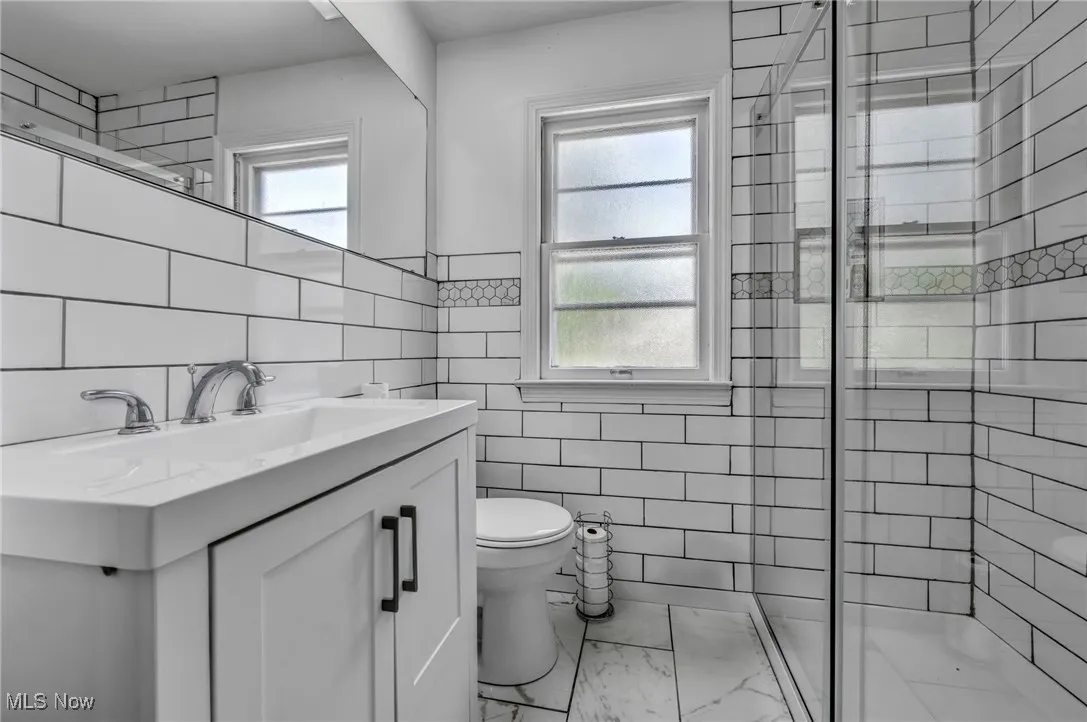 Full bathroom featuring tile walls, a shower stall, vanity, marble finish flooring, and wainscoting