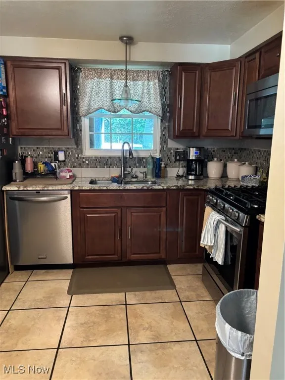 Kitchen featuring decorative backsplash, dishwasher, range, light tile patterned floors, and dark brown cabinetry
