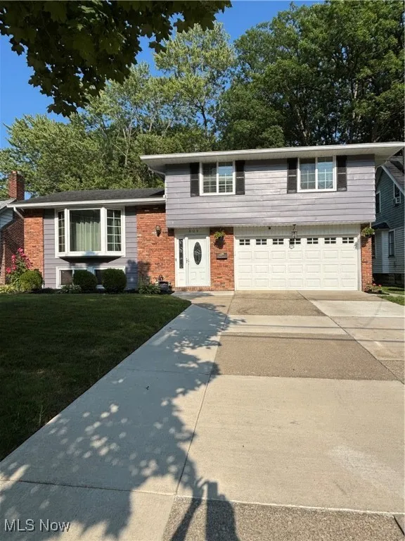 Split level home with brick siding, driveway, an attached garage, and a front yard
