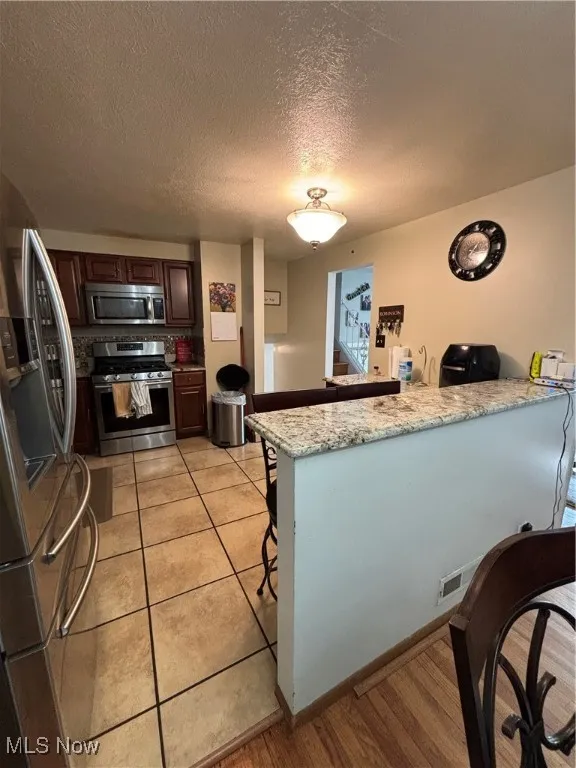 Kitchen with a peninsula, stove, refrigerator, a kitchen breakfast bar, and dark brown cabinetry