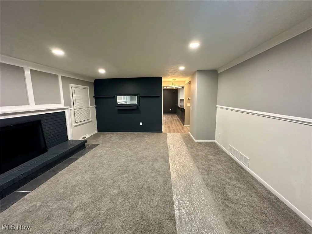 Unfurnished living room featuring carpet floors, recessed lighting, a fireplace, and ornamental molding