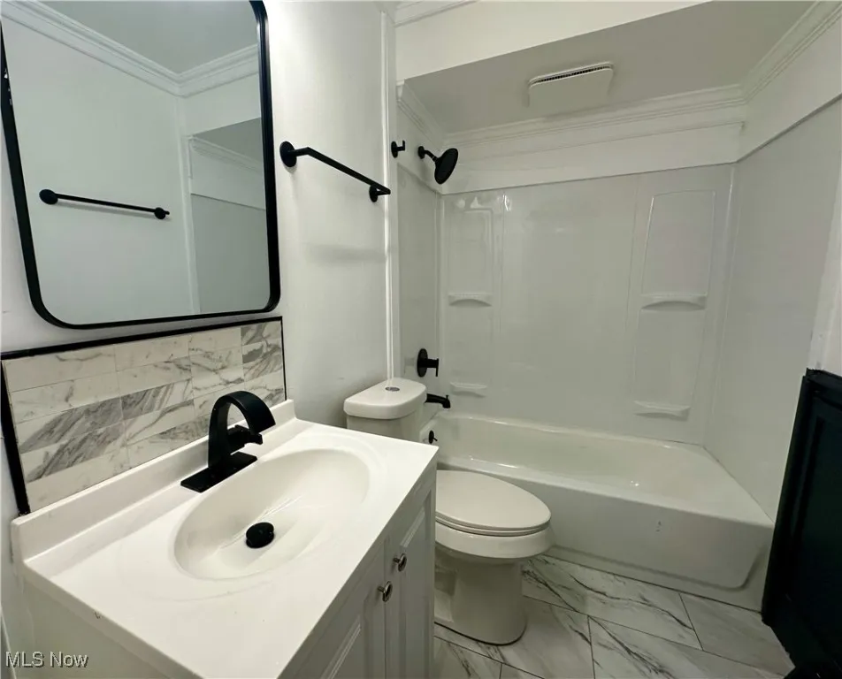 Bathroom with crown molding, marble look tiles, vanity, bathing tub / shower combination, and decorative backsplash