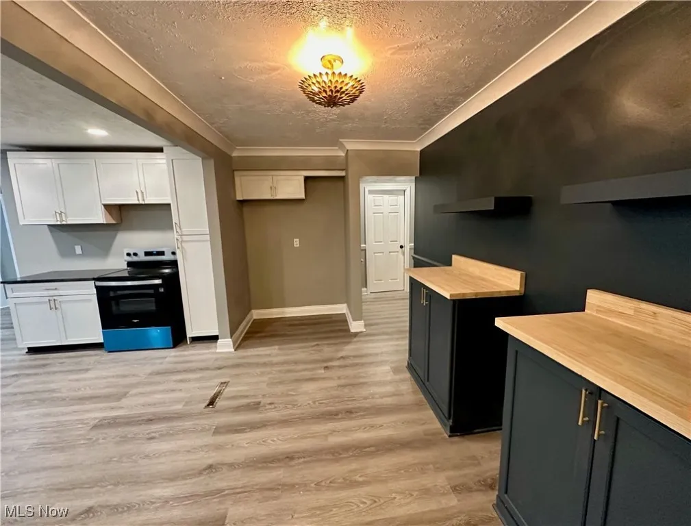 Kitchen with stainless steel electric range oven, light wood finished floors, a textured ceiling, white cabinetry, and wooden counters