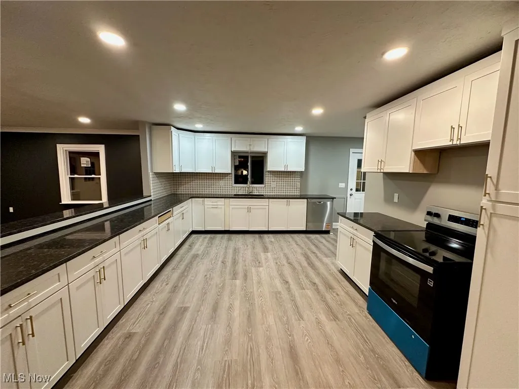 Kitchen with electric range oven, light wood finished floors, white cabinets, recessed lighting, and backsplash