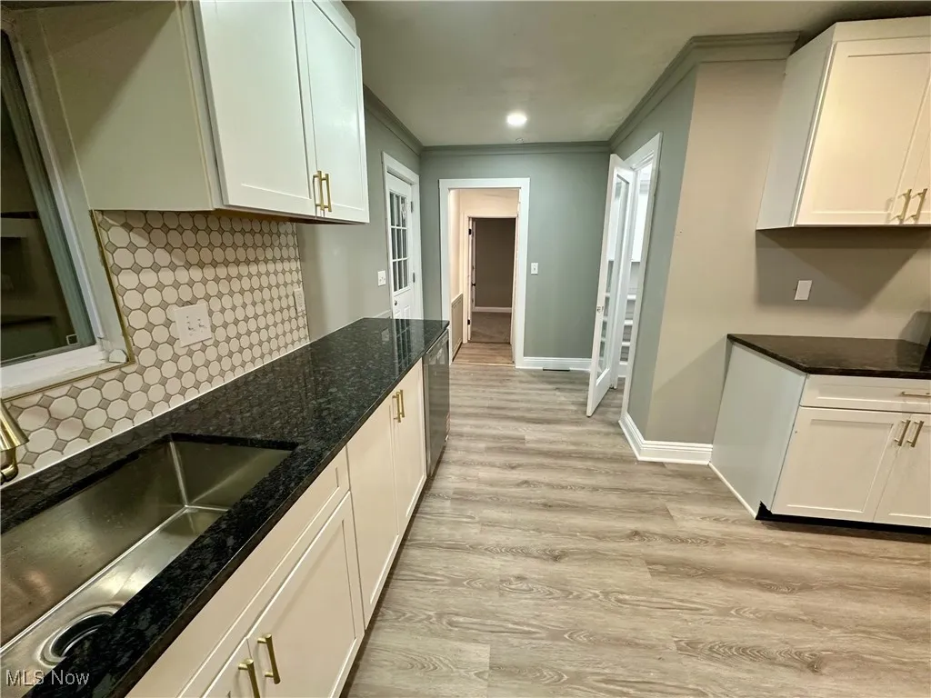 Kitchen featuring tasteful backsplash, ornamental molding, light wood-style floors, dark stone counters, and white cabinetry