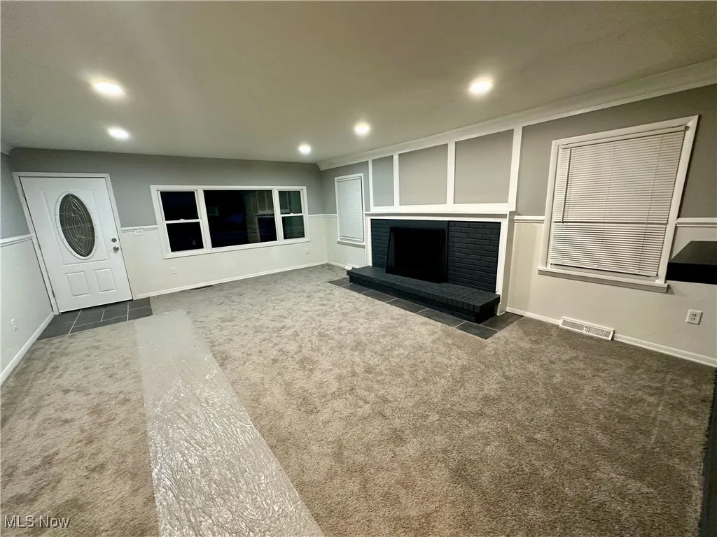 Unfurnished living room featuring recessed lighting, dark carpet, a brick fireplace, and ornamental molding