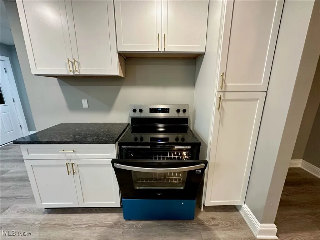 Kitchen with electric stove, wood finished floors, dark stone counters, and white cabinetry