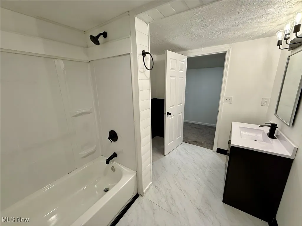 Full bath featuring shower / bathtub combination, vanity, a textured ceiling, and marble look tile flooring