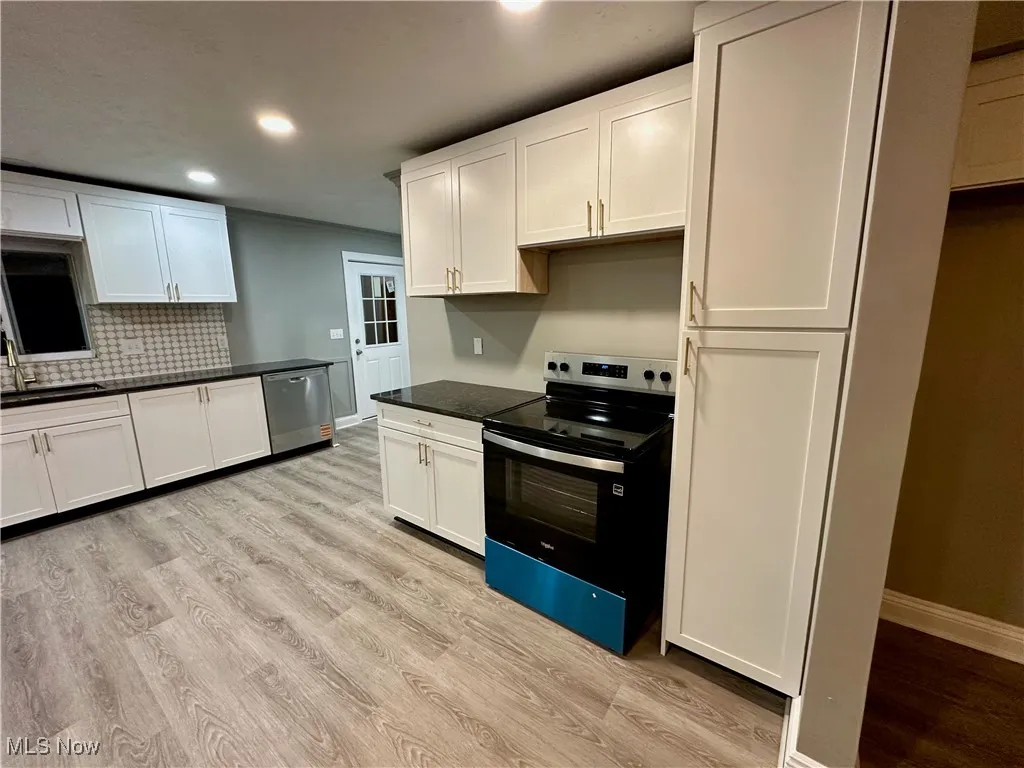 Kitchen featuring electric stove, recessed lighting, dark countertops, dishwasher, and white cabinetry