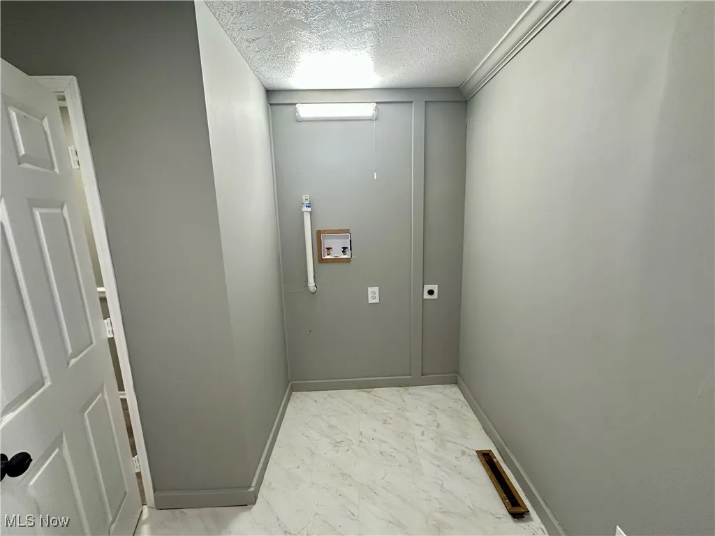 Laundry room featuring a textured ceiling, hookup for a washing machine, light marble finish floors, electric dryer hookup, and crown molding