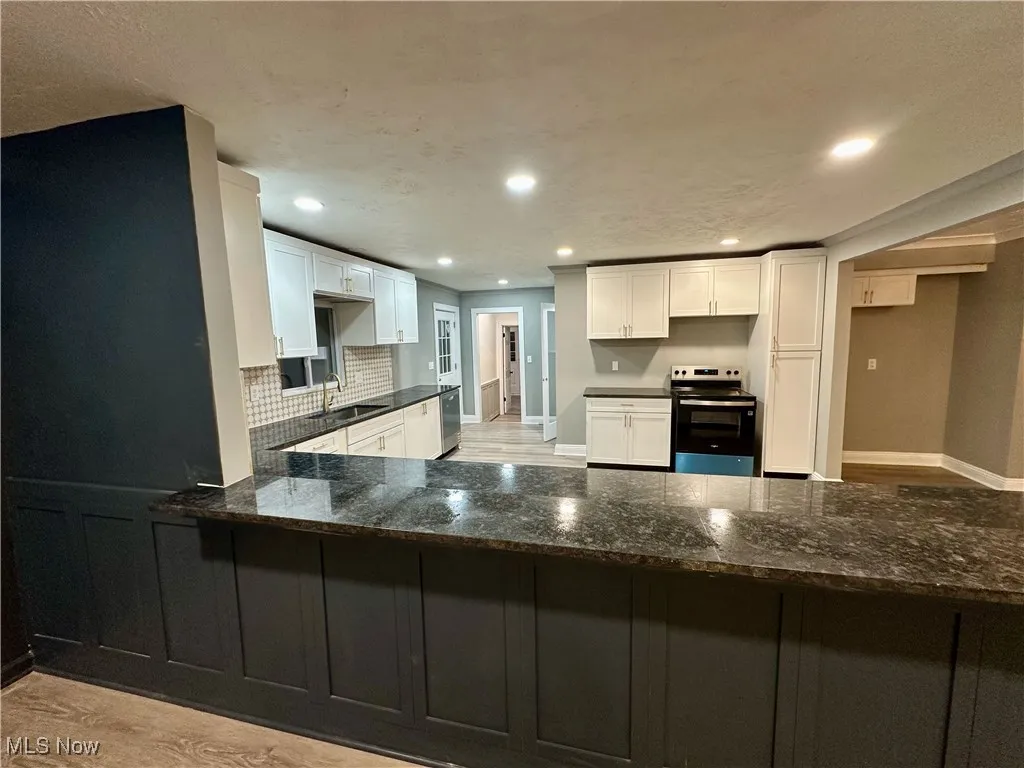 Kitchen with light wood-type flooring, appliances with stainless steel finishes, recessed lighting, dark stone countertops, and white cabinetry