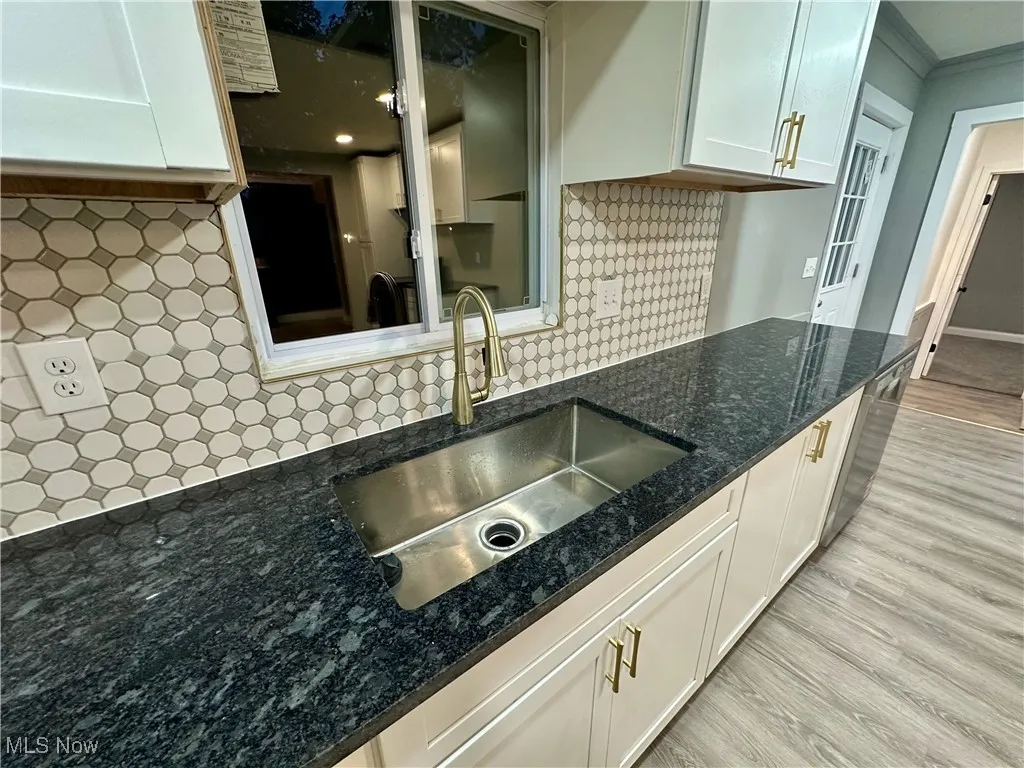 Kitchen featuring decorative backsplash, white cabinets, light wood-style flooring, dark stone countertops, and stainless steel dishwasher