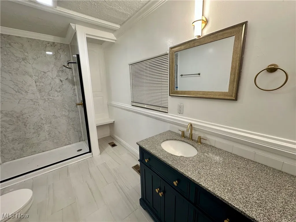 Bathroom with a stall shower, vanity, ornamental molding, and a textured ceiling