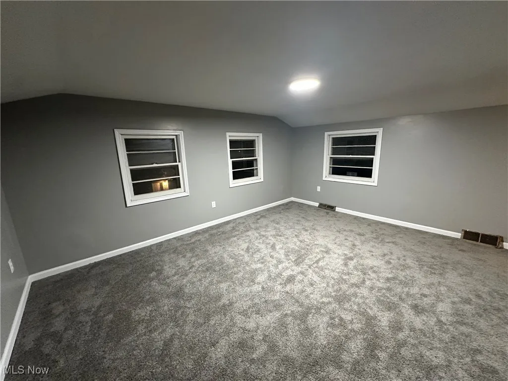 Empty room featuring lofted ceiling, dark colored carpet, and built in shelves