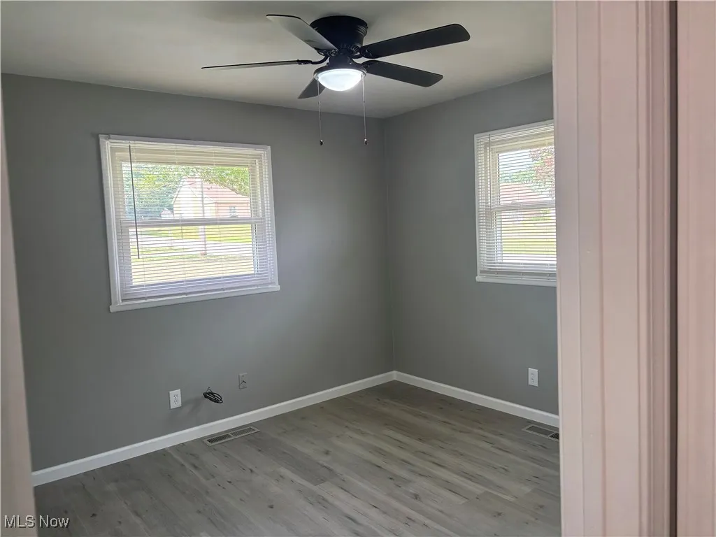 Unfurnished room with wood finished floors, plenty of natural light, and a ceiling fan