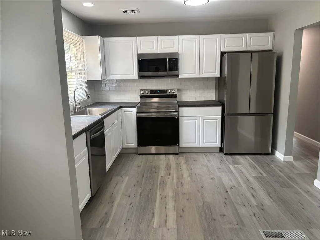 Kitchen with appliances with stainless steel finishes, backsplash, white cabinets, dark countertops, and recessed lighting