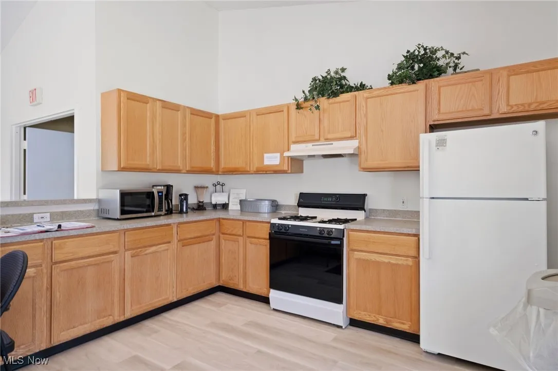 Kitchen featuring gas stove, freestanding refrigerator, light brown cabinets, and a towering ceiling