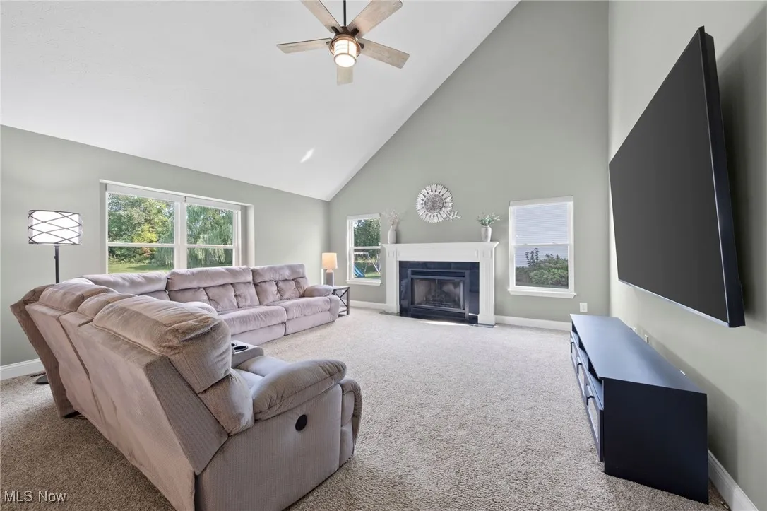 Living area featuring high vaulted ceiling, light carpet, marble fireplace  and ceiling fan