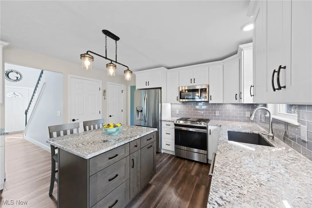 Kitchen featuring stainless steel appliances, white cabinetry, LVT flooring, a kitchen island w seating and decorative backsplash