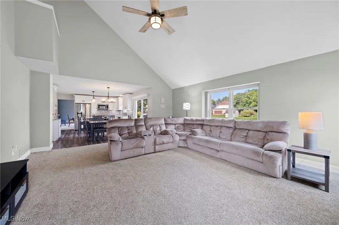 Living room featuring dark colored carpet, healthy amount of natural light, high vaulted ceiling, a ceiling fan, and a chandelier