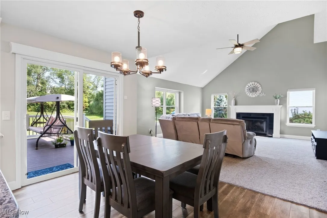 Dining area looking to deck and high vaulted ceiling family room / LVT  wood finished floors, a chandelier, and a ceiling fan