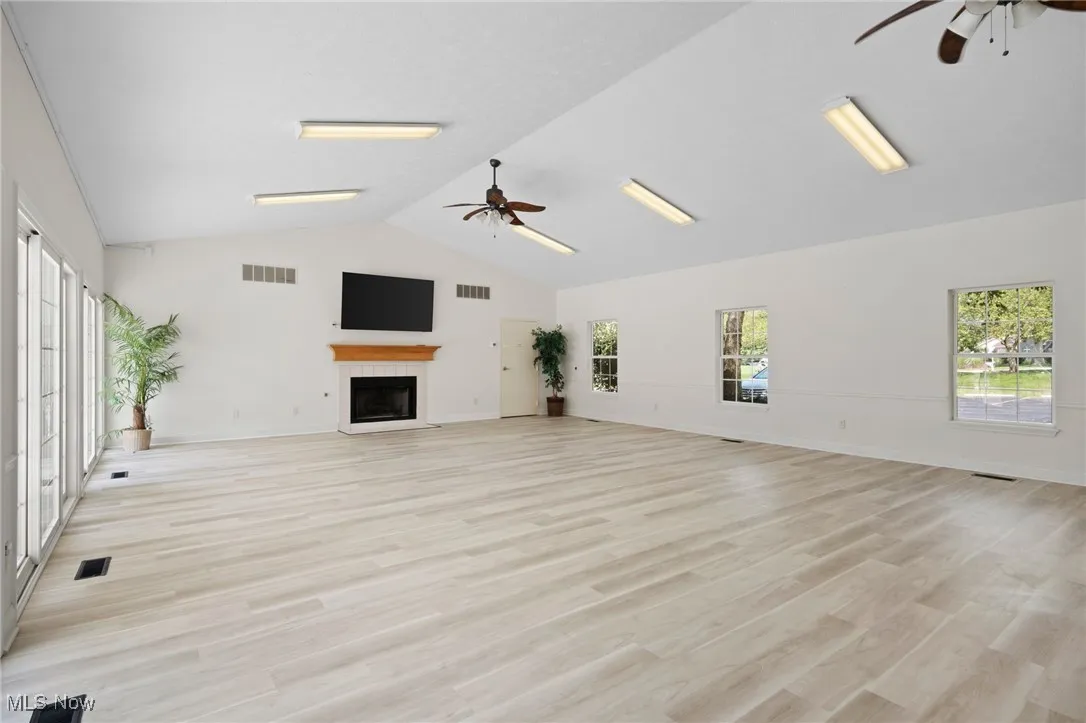 Clubhouse community room with ceiling fans, a fireplace, light wood-style flooring, and high vaulted ceiling