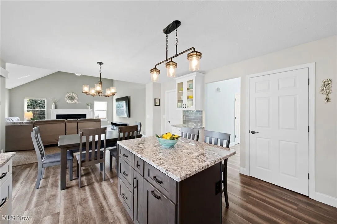 Kitchen with a island w breakfast bar, LVT flooring, white cabinetry, decorative light fixtures, and glass insert cabinets