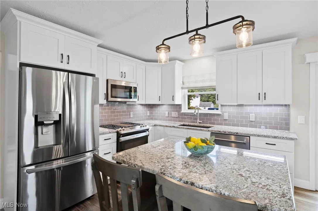 Kitchen with stainless steel appliances, decorative backsplash, white cabinetry, a center island, and a kitchen breakfast bar