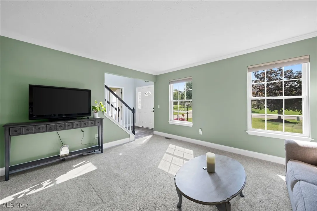 Living area featuring carpet flooring view to foyer and crown molding