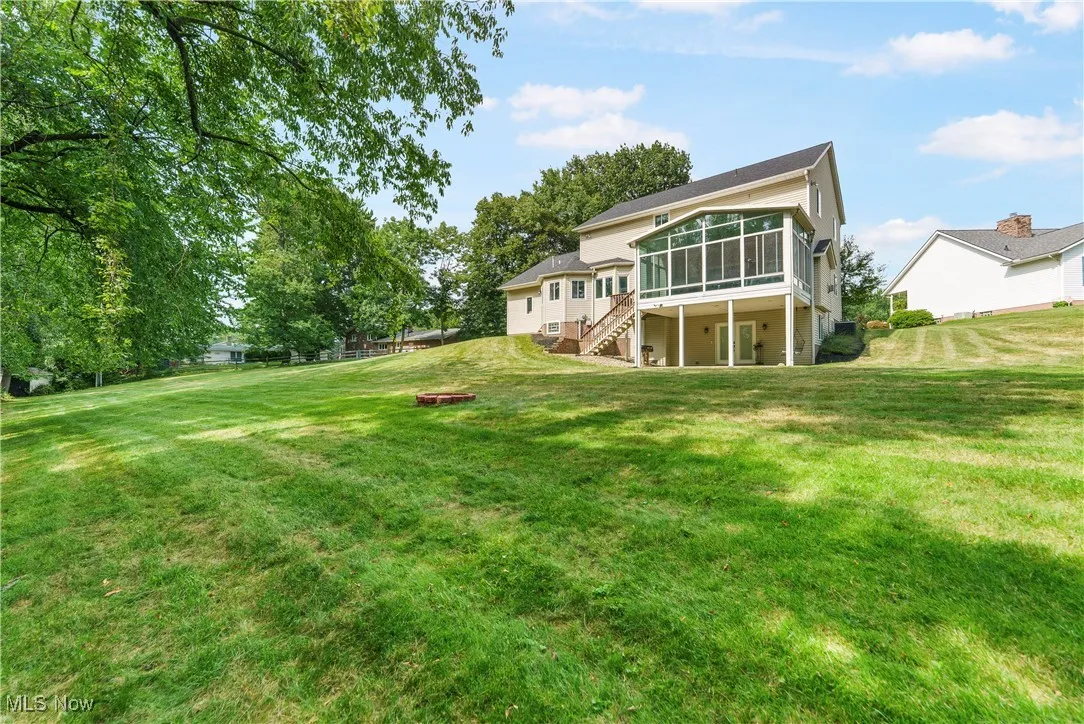 Back of house with a sunroom, stairs, a fire pit, and a lawn