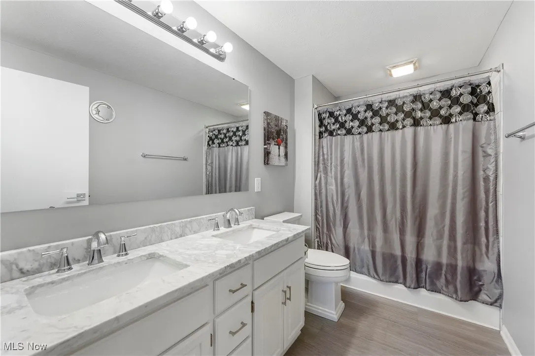 Bathroom with double vanity, shower / bath combo, wood finished floors, and a textured ceiling