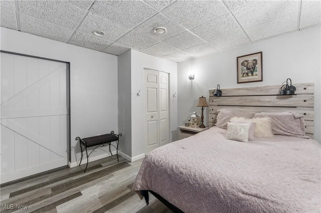 Bedroom with a drop ceiling, wood finished floors, and a closet