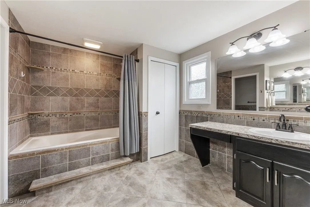 Full bathroom featuring tile walls, tiled shower / bath combo, vanity, tile patterned flooring, and a wainscoted wall