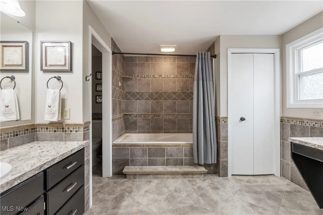 Bathroom featuring vanity, tile walls, wainscoting, tiled shower / bath, and tile patterned floors
