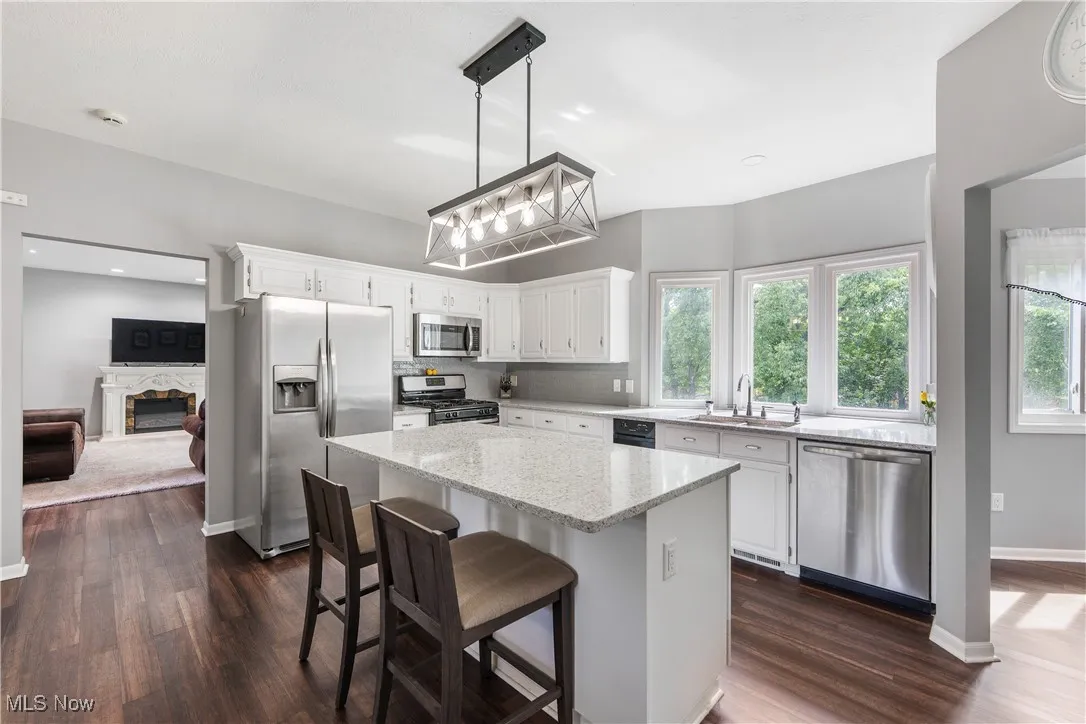 Kitchen featuring appliances with stainless steel finishes, a premium fireplace, white cabinetry, light stone countertops, and recessed lighting