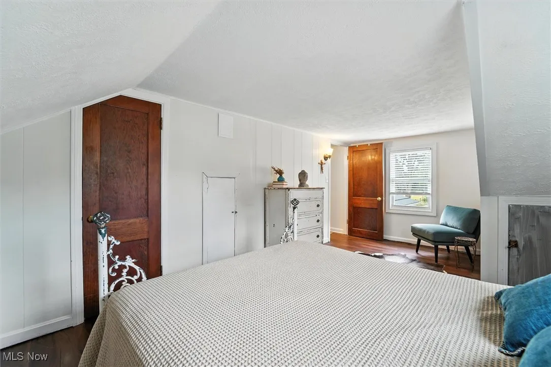 Bedroom with a textured ceiling, dark wood-type flooring, and lofted ceiling
