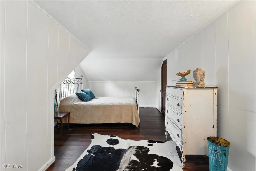 Bedroom with dark wood-type flooring, vaulted ceiling, a textured ceiling, and a decorative wall