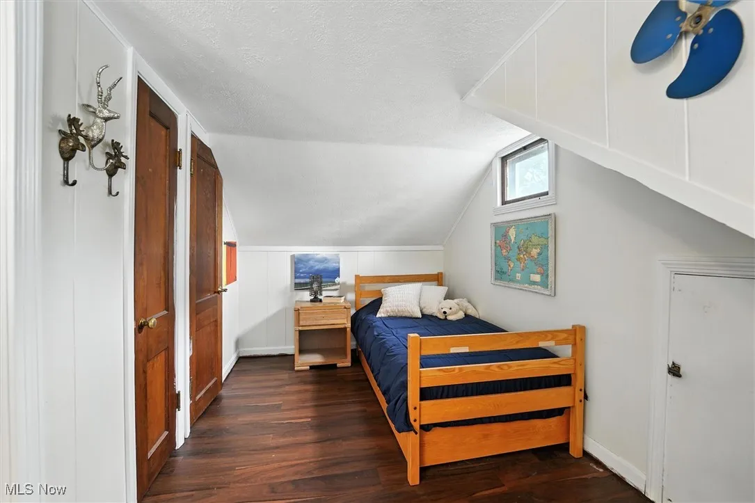 Bedroom with wood finished floors, a textured ceiling, and lofted ceiling