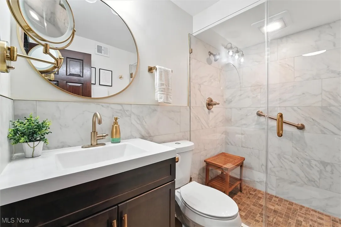 Full bath featuring a shower stall, tile walls, and vanity