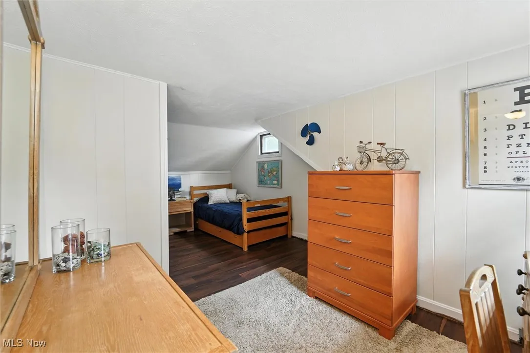 Bedroom featuring wood finished floors, lofted ceiling, and a decorative wall