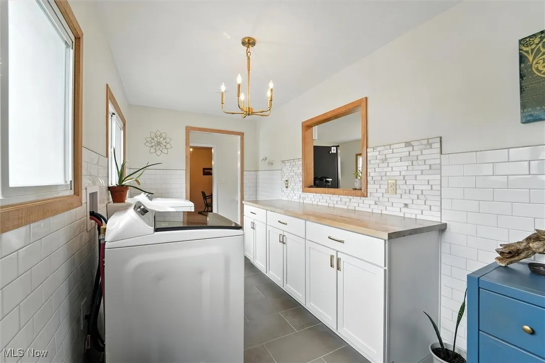 Washroom with washer and clothes dryer, tile walls, wainscoting, dark tile patterned floors, and cabinet space