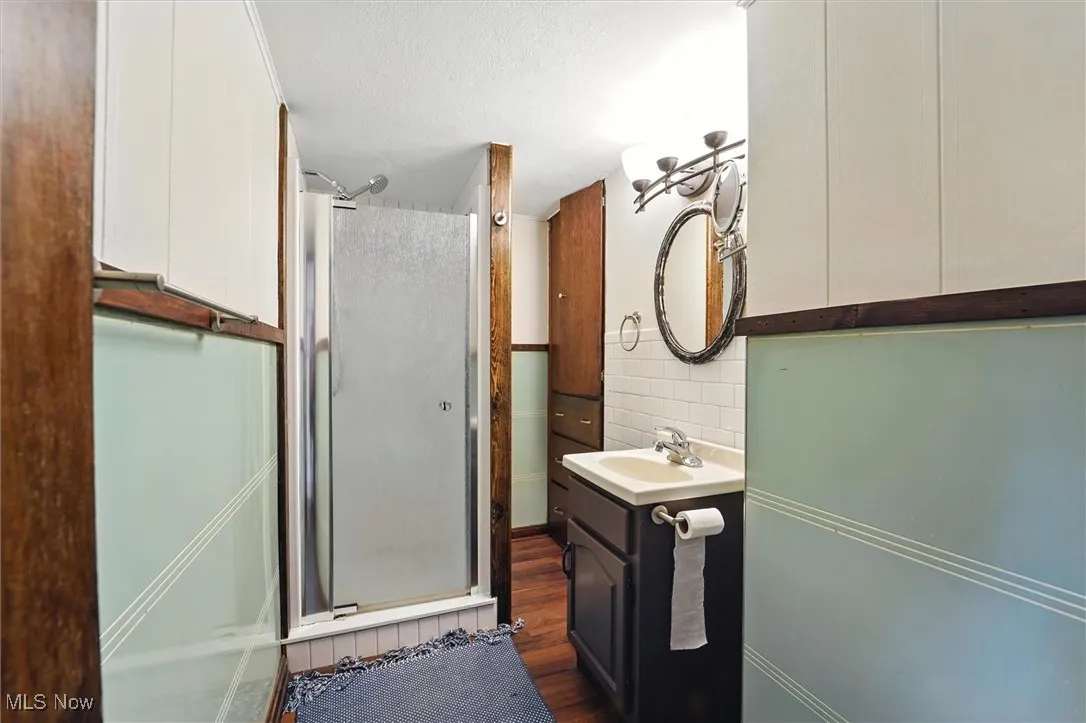 Full bathroom featuring a stall shower, vanity, wood finished floors, and decorative backsplash
