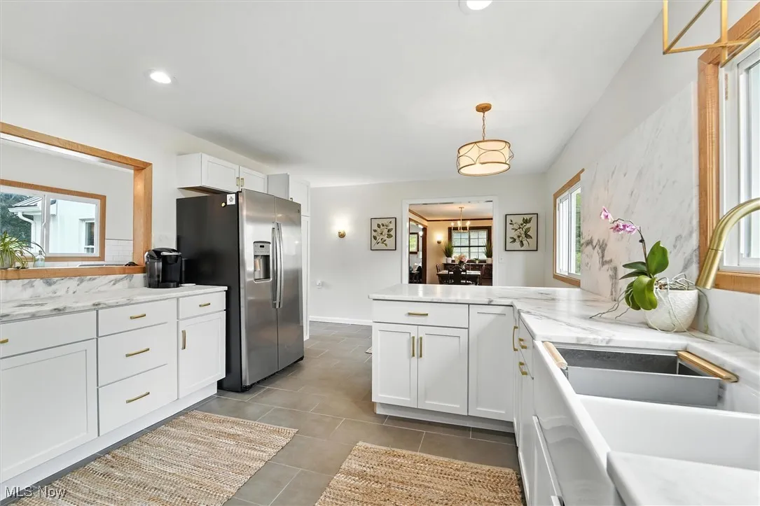 Kitchen with stainless steel fridge, white cabinetry, a peninsula, hanging light fixtures, and recessed lighting