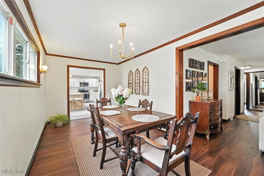 Dining space with dark wood-style flooring, a chandelier, and ornamental molding